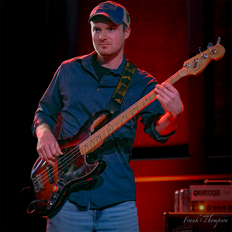 Alex Degnan looks down as he holds a bass guitar
