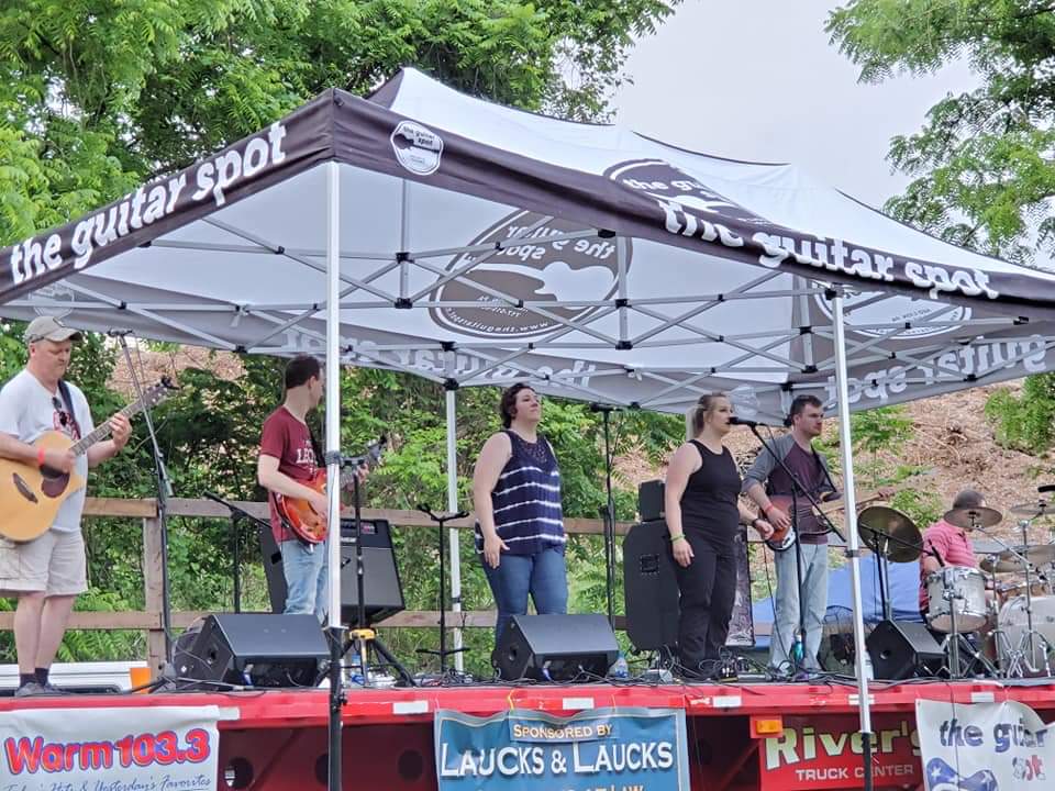 a band wearing summer clothes stands under tents on an outdoor stage