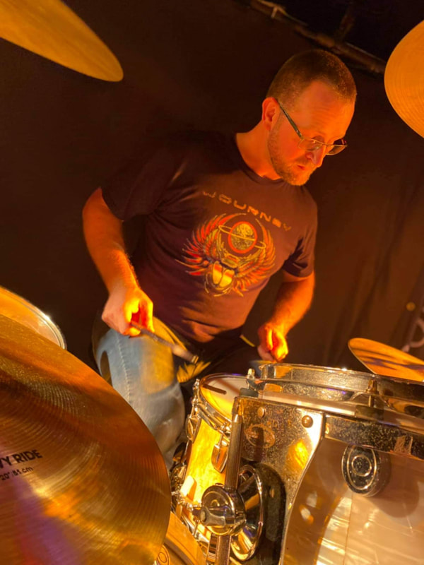 A male drummer in a Journey t shirt plays the snare drum