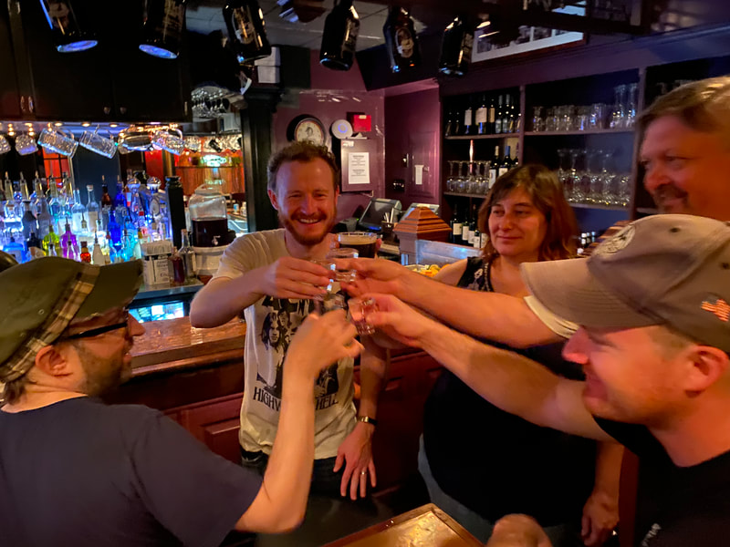 a circle of band mates raise a toast and clink shot glasses in an Irish pub