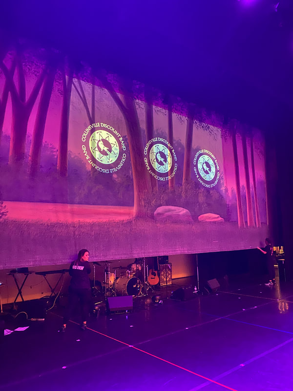 a stage "cyc" is with a forest scene and band logo overlay