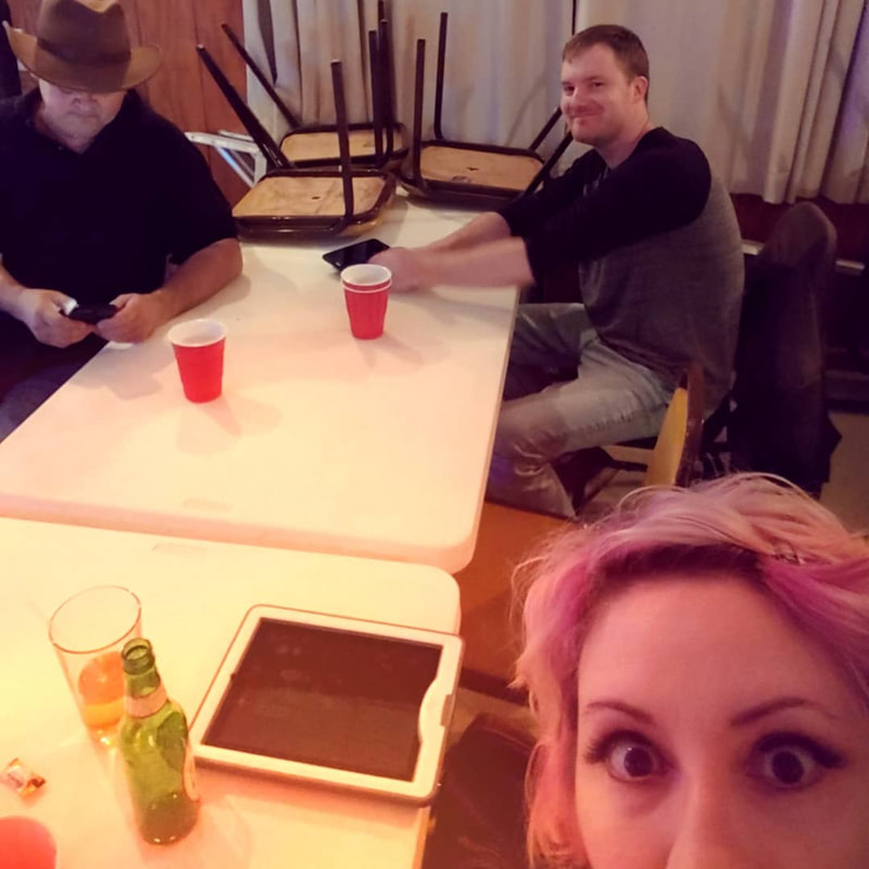 two males and a female band mate smile while sitting at a table with drinks.