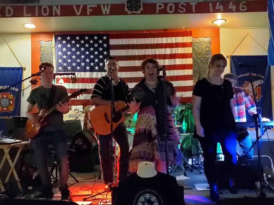 a mixed gender band performs in front of an American flag