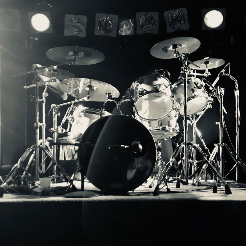 a rock drum kit twinkles under hot stage can lights.