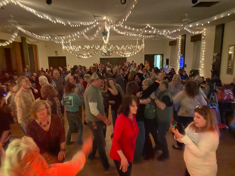 A thick crowd of adults fills a dance floor under ballroom lights