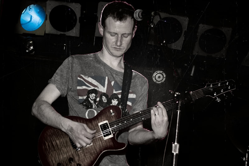 a male guitarist in a Queen t shirt plays an electric guitar